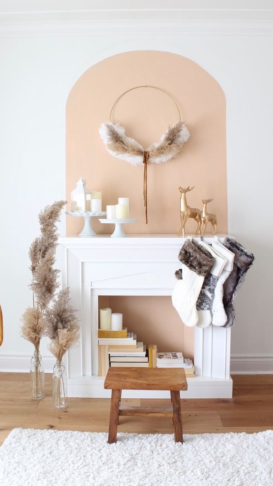 a faux fireplace with a peachy inside, books and candles and stockings and a wreath for Christmas