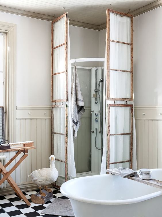 a vintage bathroom with a modern shower space but clad with old window frames and with white fabric hanging