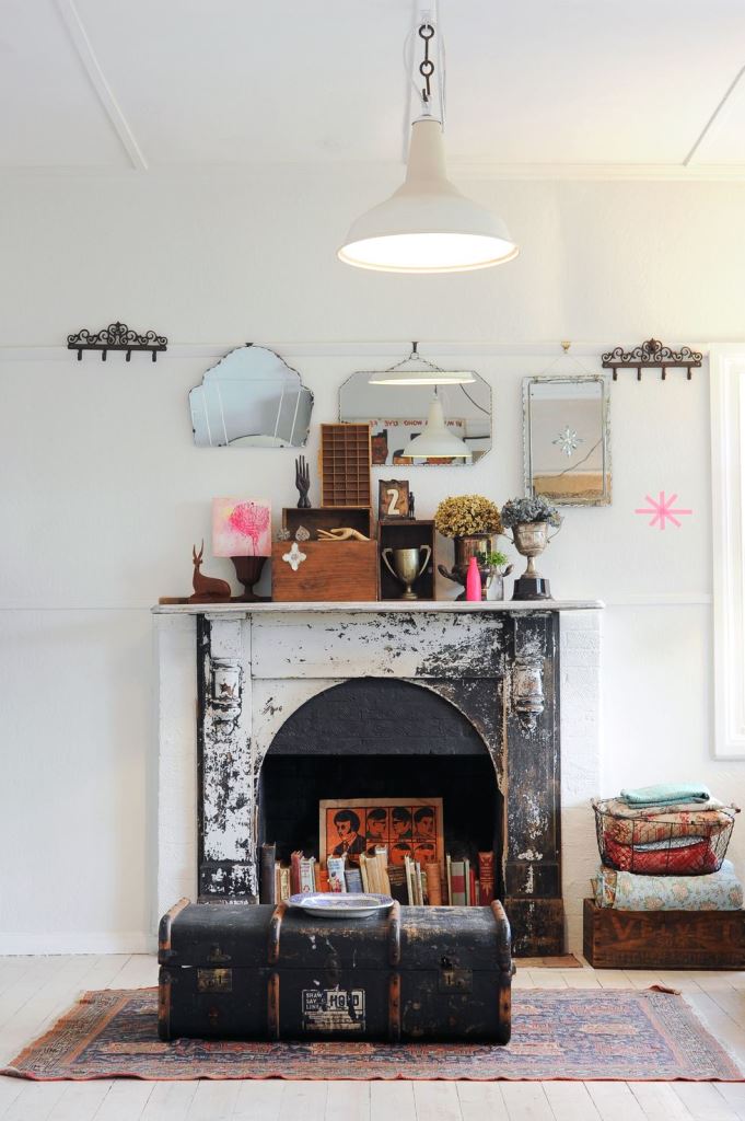 A shabby cihc fireplace with books and a bold artwork looks statement like and bold, a suitcase in front of it adds vintage charm