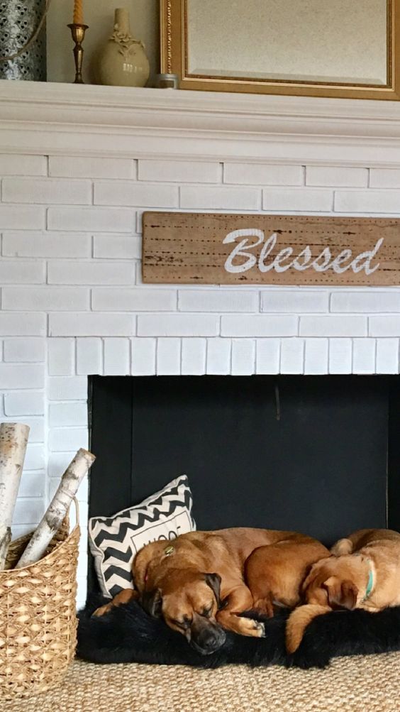 A non working fireplace with white brick and a furry bed for two dogs inside it, with pillows