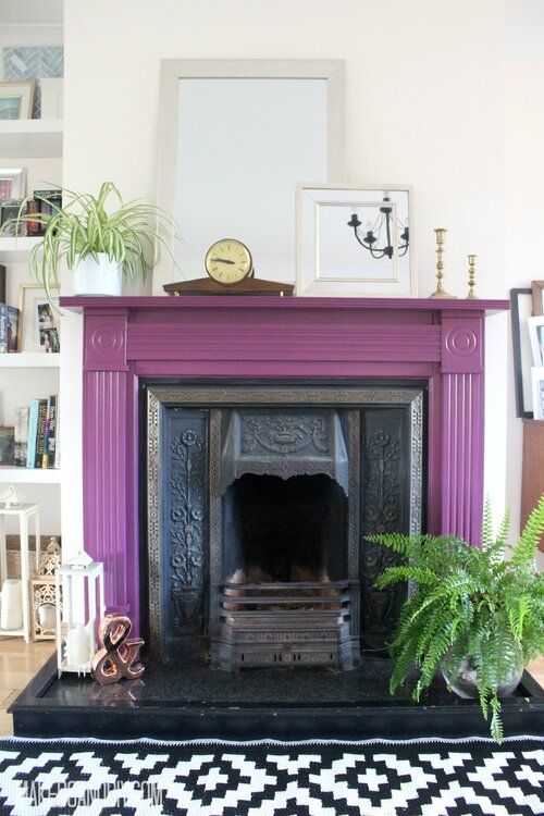 a vintage fireplace with a purple mantel around, some potted plants, candle lanterns and mirrors