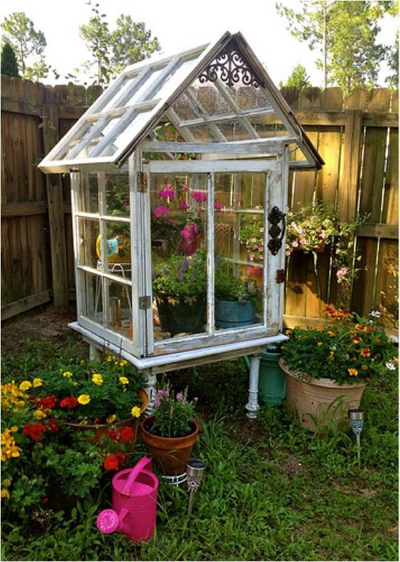 a large greenhouse with lots of planters built completely of old window frames and with bright blooms inside is very nice for outdoors