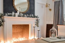 26 a winter non-working fireplace with lights inside it, snowy fir garland, candles and a mirror over the mantel