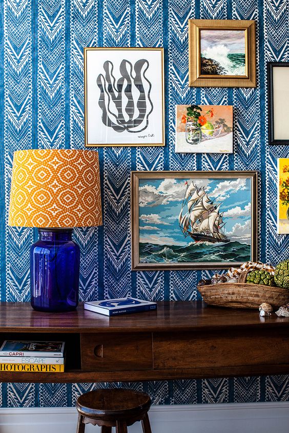 Refined bold blue and white printed wallpaper and a gallery wall on it plus a printed lamp for a bright and eye catchy nook