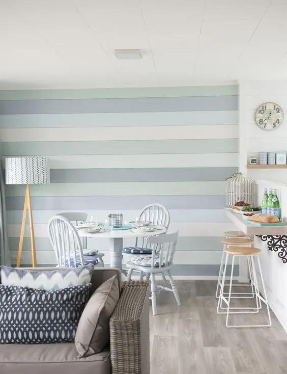 A beach space with a small breakfast bar, a dining space and a living room and a coastal colored accent wall for a statement