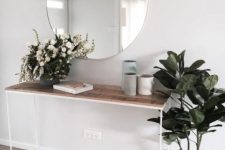 a chic modern entry with a wooden console, a round mirror and some potted plants and vases