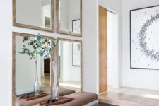 a chic modern entryway with a gallery wall of mirrors, a leather and acrylic bench and greenery in a vase