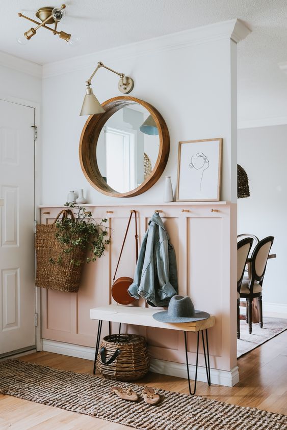 a chic modern entryway with a pink paneled wall, a round mirror, a pinhair leg bench and baskets