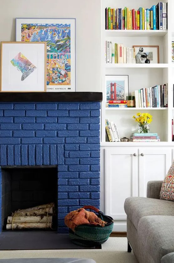 A chic modern living room with a grey sofa, a navy brick fireplace, built in shelves and a cabinet and some bold artwork