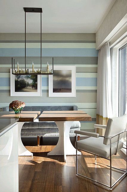 a coastal dining room with a unique striped wall in coastal colors, neutral furniture, color block curtains and a unique chandelier