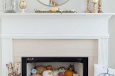a contemporary fireplace with colorful pumpkins inside, firewood and a blue pumpkin pillow plus some leaves on the mantel