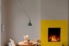 a contemporary space with dove grey walls and a checked floor, a fireplace accented with a bit of yellow paint, firewood, a cool wall lamp and some books
