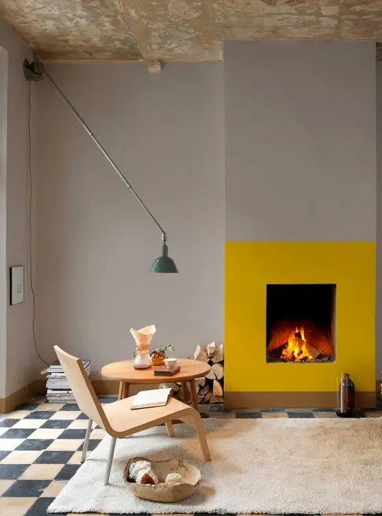 a contemporary space with dove grey walls and a checked floor, a fireplace accented with a bit of yellow paint, firewood, a cool wall lamp and some books