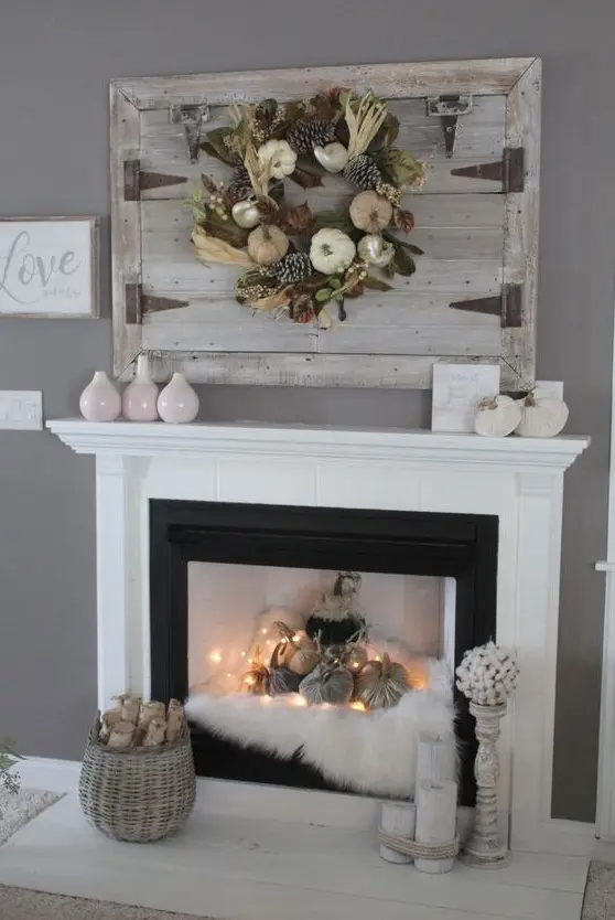 a fall fireplace styled with faux fur, fabric pumpkins and lights, a basket with firewood, candles and vases is a beautiful idea