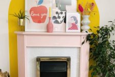 a fireplace with a blush mantel and a bold yellow accent on the wall plus bright decor on the mantel is cool