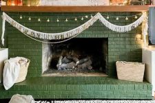 a green brick fireplace with lights and a garland, with decor, candles and artwork is a cool and lovely decoration