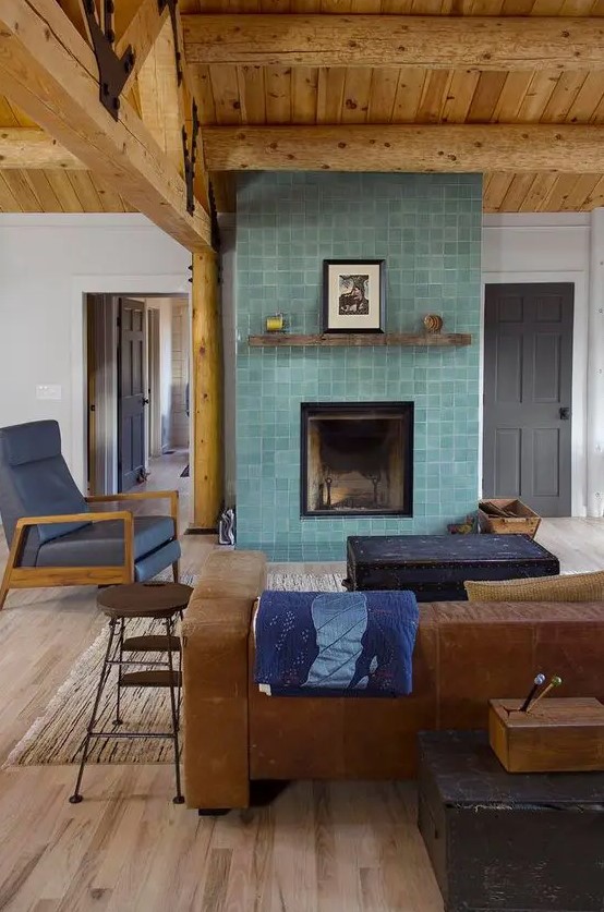 A living room with a stained ceiling, a leather sofa and a fireplace clad with aqua colored Zellige tiles