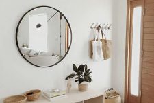 a modern entry with a sleek bench, a round mirror, some baskets and a clothes rack is stylish and looks ethereal