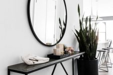 a modern entryway with a black narrow console, a round mirror, a statement plant and some decor
