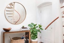 a modern entryway with a wooden sleek console, a round mirror, some baskets and a statement plant