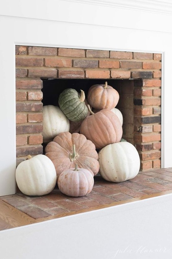A modern fireplace with neutral and pastel pumpkins is a cool idea for a modern fall embracing space and is an easy to realize decor idea