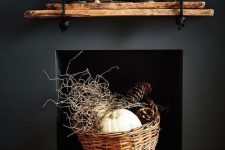 a modern rustic and woodland decoration – a black built-in fireplace with a basket with twigs, pumpkins and large pinecones is awesome for fall