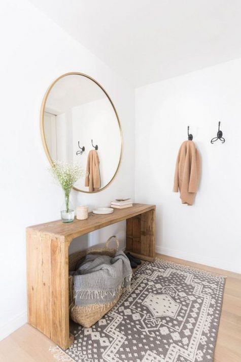 A modern warm colored entry with a wooden bench, a round mirror, a printed rug and a basket with a blanket