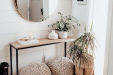 a neutral modern entryway with a wooden console, crochet ottomans, potted plants and a round mirror is chic