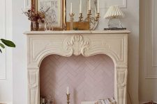 a non-working French fireplace with blush herringbone tiles inside, books, a candle in the candleholder and some vintage decor on the mantel