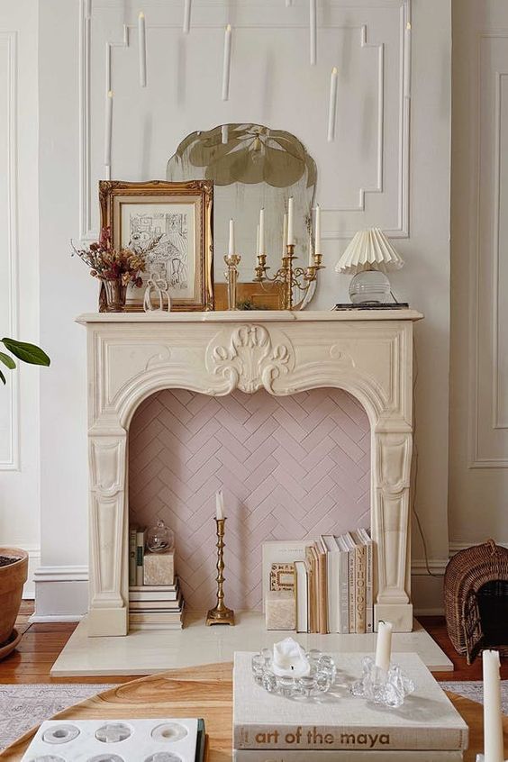 a non-working French fireplace with blush herringbone tiles inside, books, a candle in the candleholder and some vintage decor on the mantel