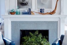 a non-working fireplace clad with blue tile, with a large seashell planter and greenery, coastal decor on the mantel