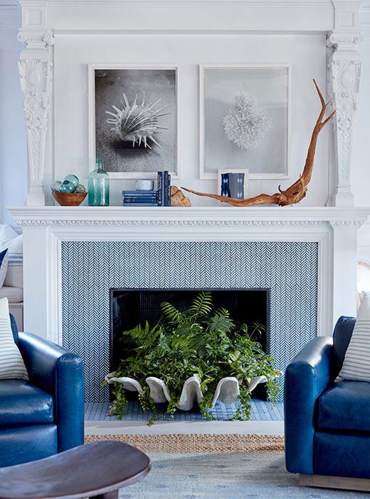 A non working fireplace clad with blue tile, with a large seashell planter and greenery, coastal decor on the mantel