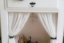 a non-working fireplace with a cozy pet bed, a toy and a chandelier plus curtains, for a little princess or prince