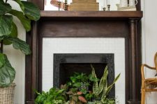 a non-working fireplace with potted greenery and succulents, boxes, candles and jugs on the mantel for a boho space