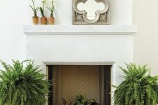 a non-working fireplace with potted plants, large ferns in planters on both sides of the fireplace, potted blooms and a mirror