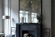 a refined living room with a black fireplace that is used for book storage and a vintage mirror for a more exquisite look in the space
