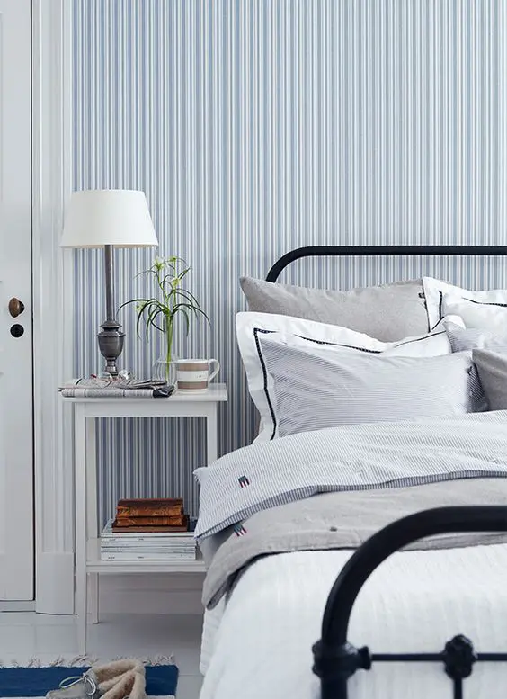 a retro coastal bedroom with a blue and white striped wall. a black metal bed and a white nightstand plus a vintage lamp