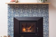 a stylish fireplace clad with blue patterned tiles around and blue glossy ones on the floor plus a simple wooden mantel is very vibrant