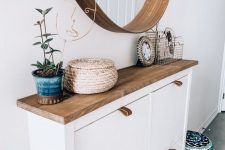 a stylish modern entry with an IKEA shoe cabinet hacked, a round mirror and a potted plant