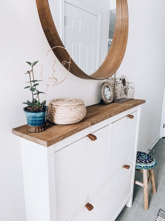 a stylish modern entry with an IKEA shoe cabinet hacked, a round mirror and a potted plant