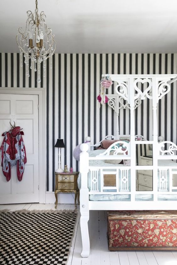 a super refined bedroom with a black and white striped wall, a unique carved bed, a beautiful crystal chandelier and exquisite furniture