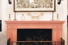 a vintage fireplace with a slamon pink mantel and a wire screen, an artwork and wall sconces is a pretty addition to your living room