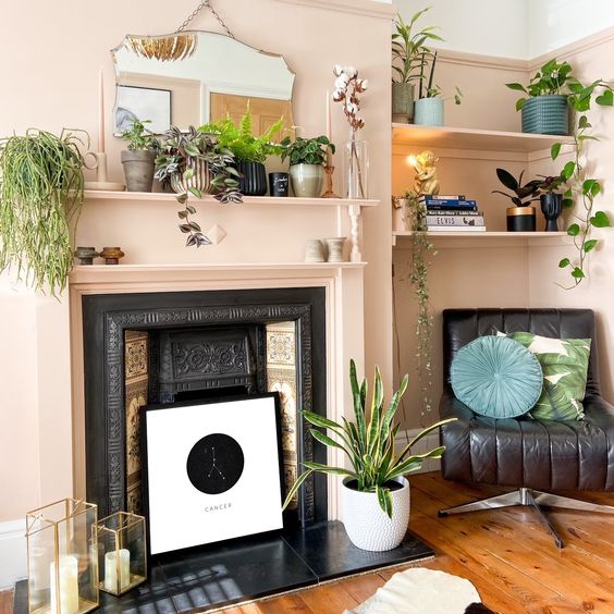 a vintage non-working fireplace with an artwork, candle lanterns and a potted plant next to it