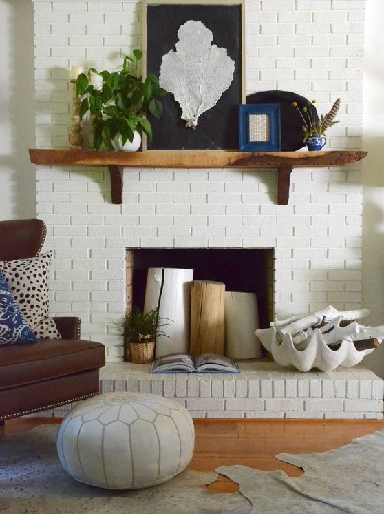 a white brick fireplace styled with tree stumps, a potted plant, a large seashell with whitewashed driftwood for summer