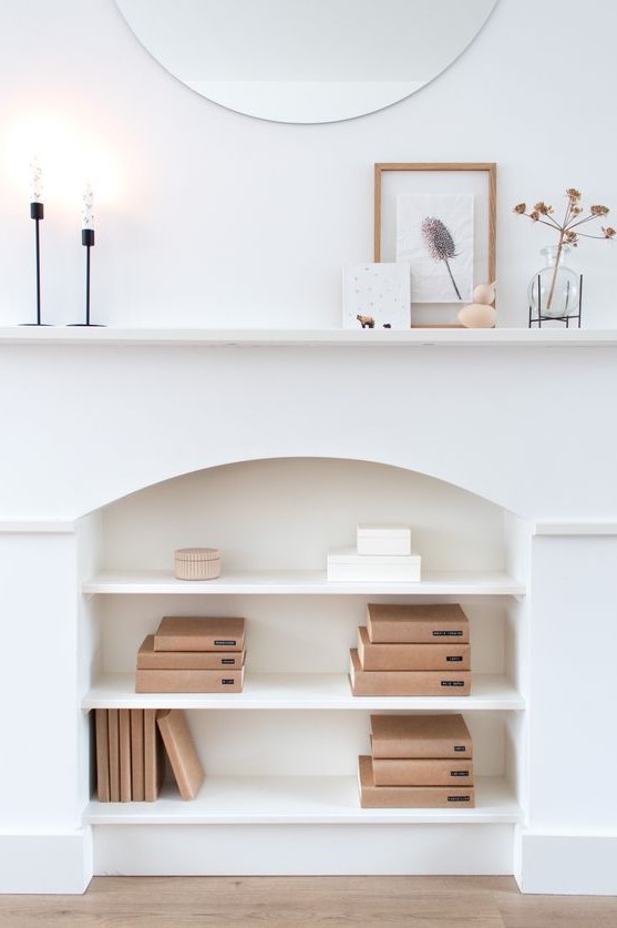 a white faux fireplace used for book storage, minimalist mantel decor with candles, herbs and a botanical artwork