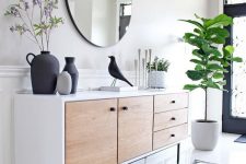 an airy modern entryway with a mid-century modern sideboard, a round mirror, a statement plant and some decor