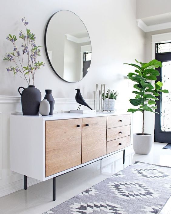 an airy modern entryway with a mid-century modern sideboard, a round mirror, a statement plant and some decor