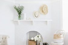 an airy space with chic chairs, a brick fireplace with a basket and white blooms, hats and vases is very cozy and welcoming