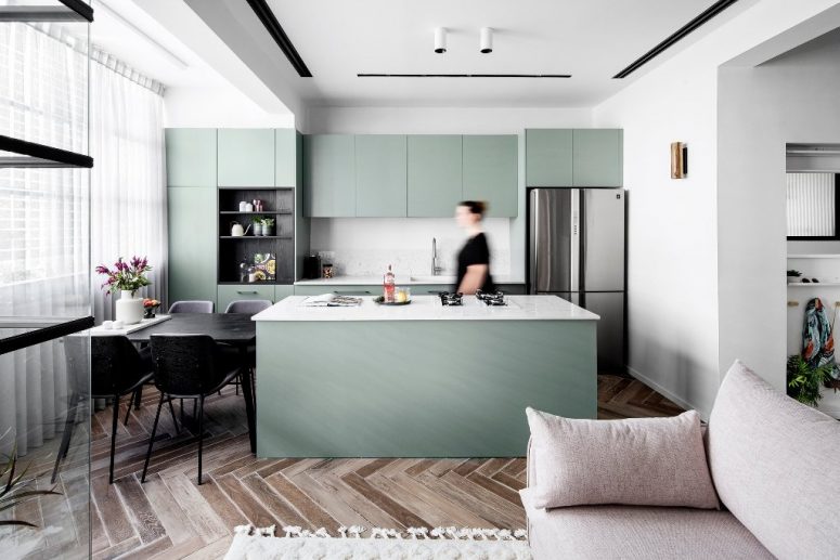The kitchen and dining zone are also here, the cabinets are green ones, with mable countertops and a backsplash, a black dining table and chairs