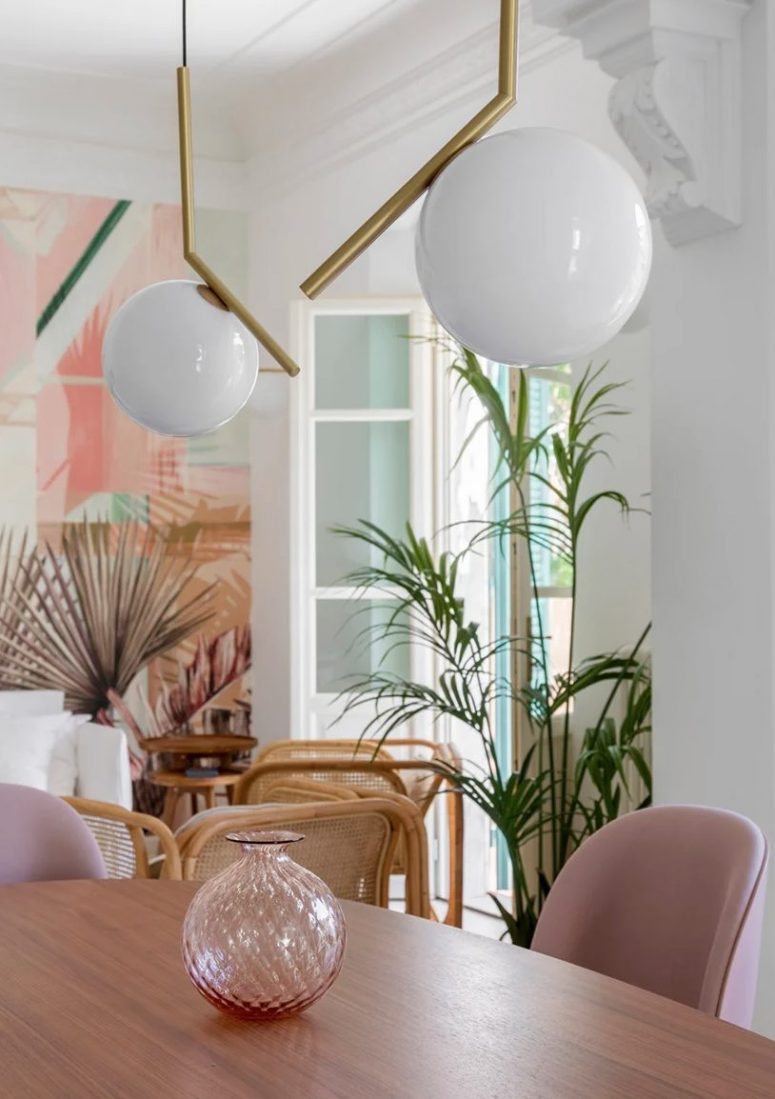 The dining space is done with an oval table, pink chairs, a pink vase and catchy pendant lamps